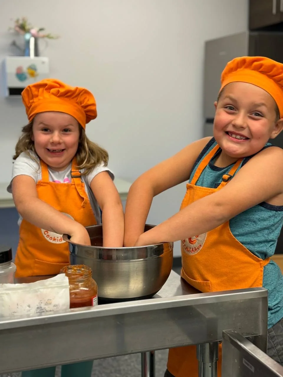 Two kids laughing while kneading dough at a Cookiddoo cooking class in Ottawa