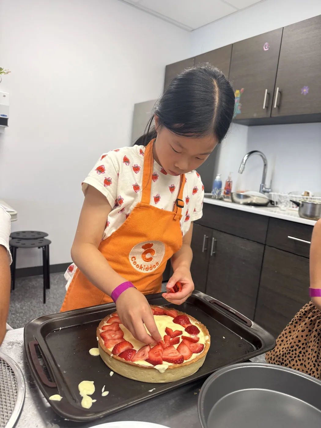 Girl in a Cookiddoo apron placing fresh strawberries on a tart during a kids baking and decorating class in Kanata