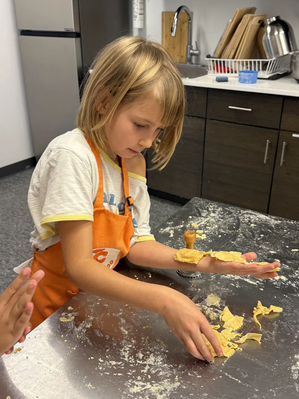 Girl in a Cookiddoo apron rolling out dough on a floured counter at a kids cooking class