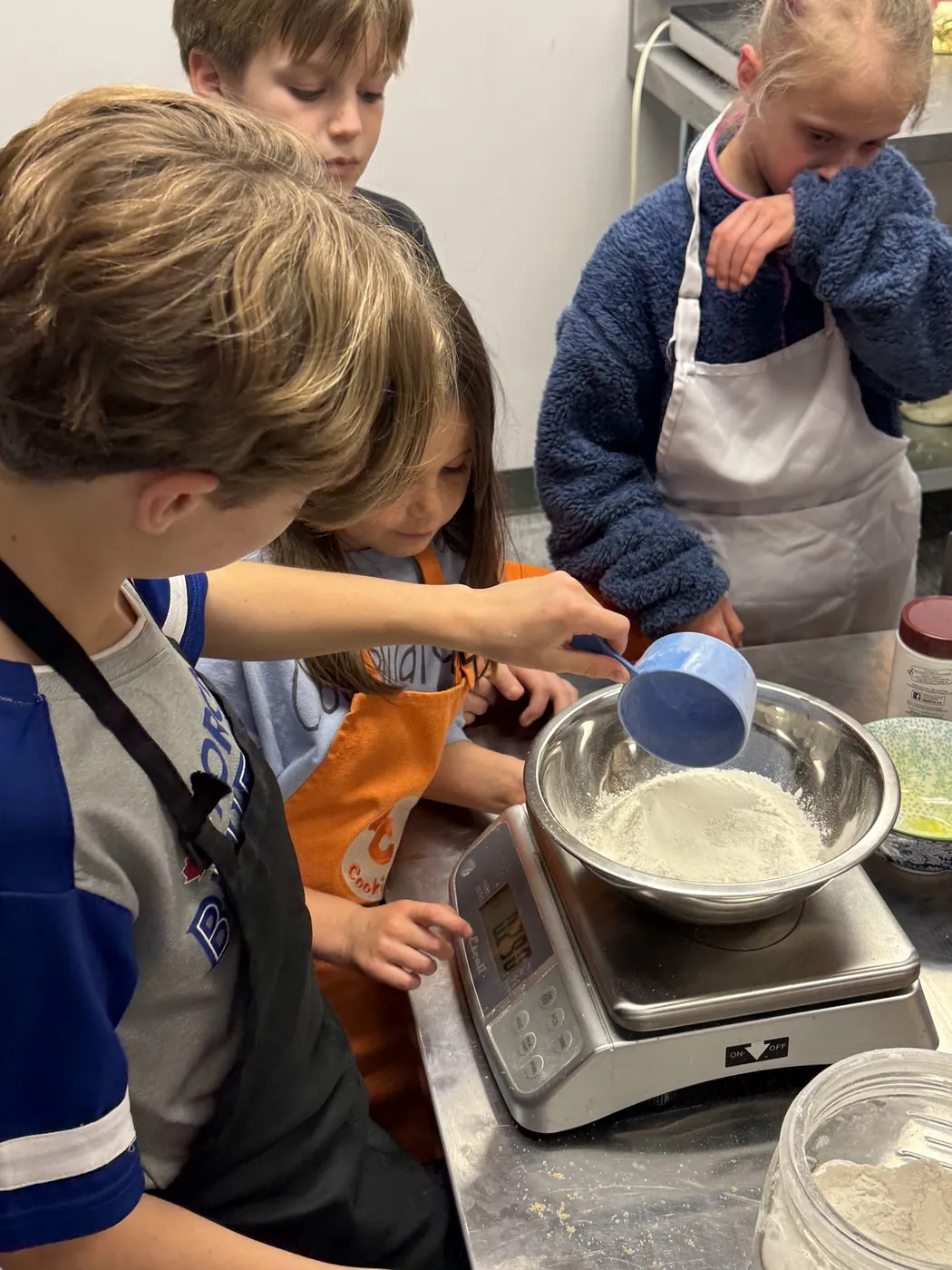 Kids measuring flour into a bowl on a kitchen scale during a Cookiddoo cooking class in Kanata