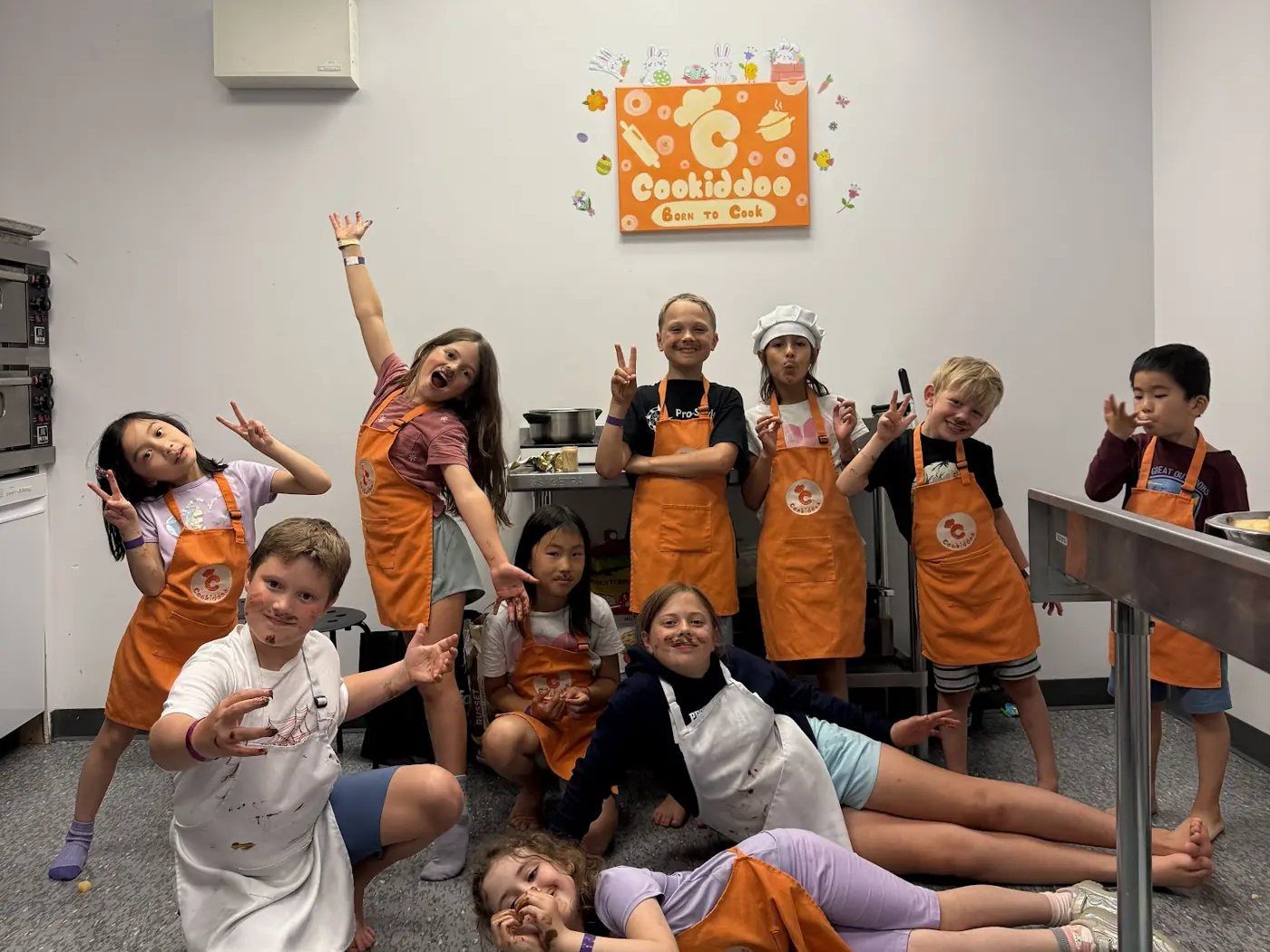 Un groupe d’enfants portant des tabliers orange Cookiddoo qui célèbrent après un cours de cuisine à Ottawa