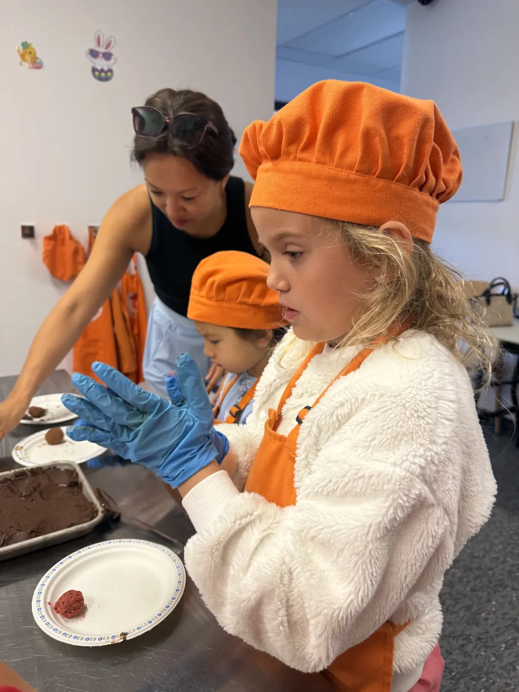 Une fillette portant un gant bleu roule des truffes au chocolat avec l’aide d’une animatrice